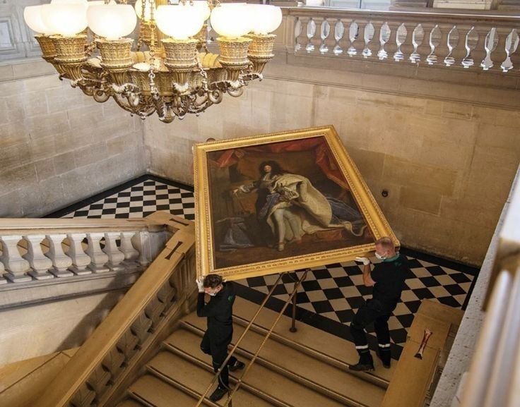 Dos montajistas trasladan una pintura enmarcada por la escalera de un museo.