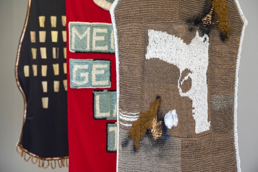Detalle de tres textiles colgantes con letras cosidas y la lana a la vista.