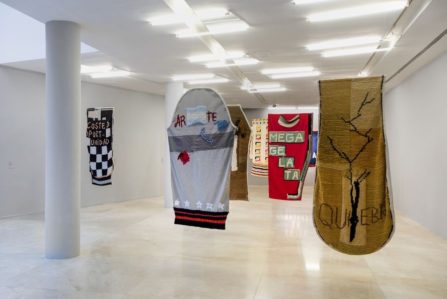 Vista de sala: tejidos con palabras cosidas cuelgan del techo en el Malba.