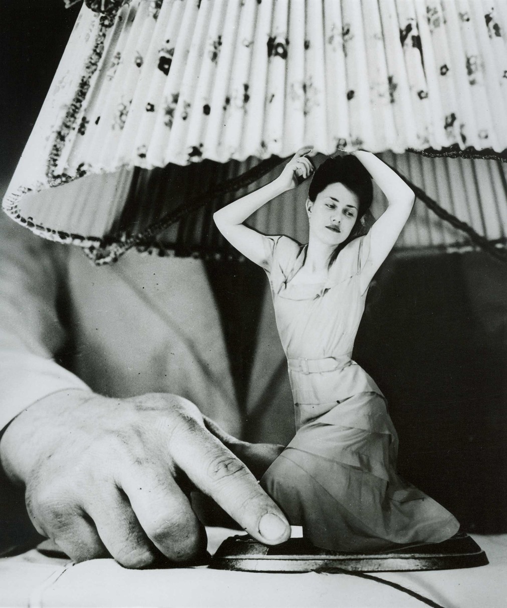 Fotomontaje de Grete Stern: una mujer arrodillada hace de pie de lámpara mientras una mano gigante alcanza el interruptor.