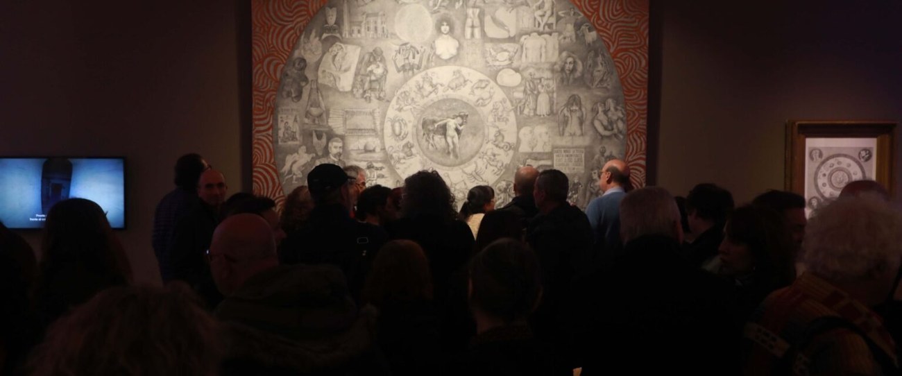 Público frente al dibujo monumental de Adriana Bustos en la sala oscura del museo.