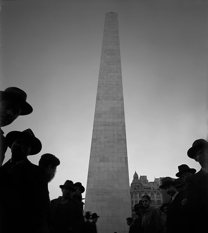 El Obelisco recién terminado, fotografiado por Horacio Coppola en 1936 entre una multitud de hombres de sombrero a contraluz.