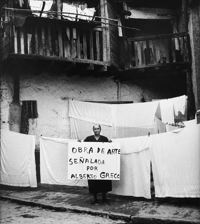 Un hombre sostiene un cartel que dice Obra de arte señalada por Alberto Greco, entre sábanas tendidas.